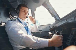 Piloto masculino al mando controlando el avión mientras ajusta el micrófono de los auriculares más cerca de su boca