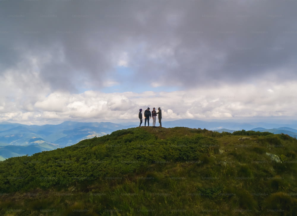 As quatro pessoas de pé em uma montanha contra a pitoresca paisagem das nuvens