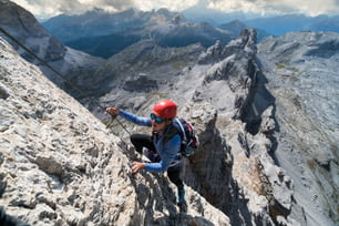 Young female climber on a steep and exposed Via Ferrata in the Italian Dolomites with a fantastic view of the surroundings