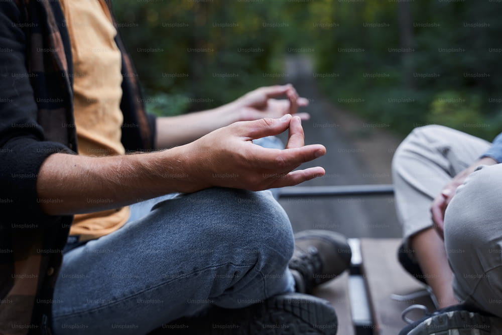 Cropped photo of happy young male sitting opposite woman and meditating while resting together outdoors. Concept of calm and meditation