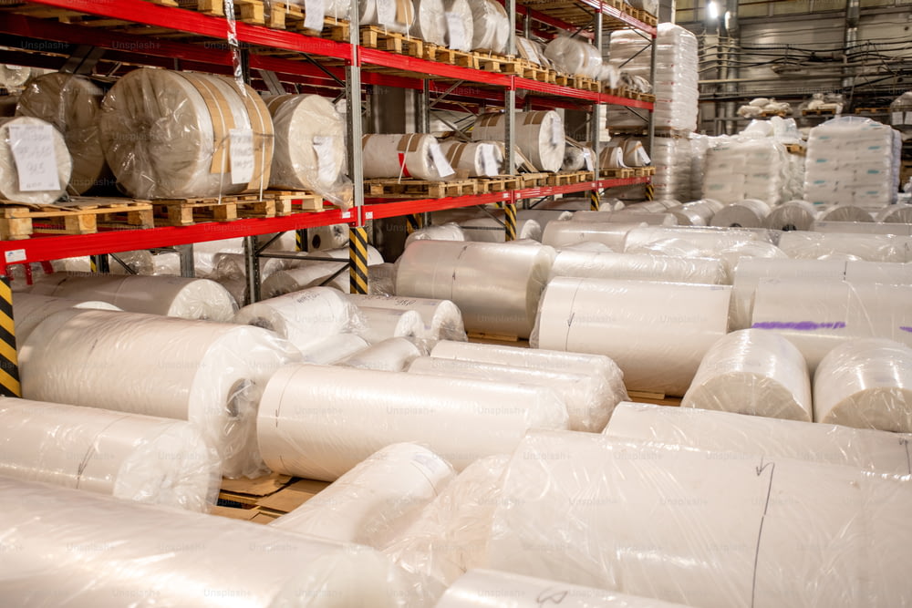 Grandi bobine arrotolate, imballate e avvolte di film di polietilene di nuova produzione all'interno del magazzino della fabbrica chimica