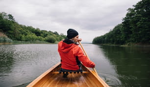 Vista traseira do homem remando canoa no lago. Passeio de barco de dia chuvoso.