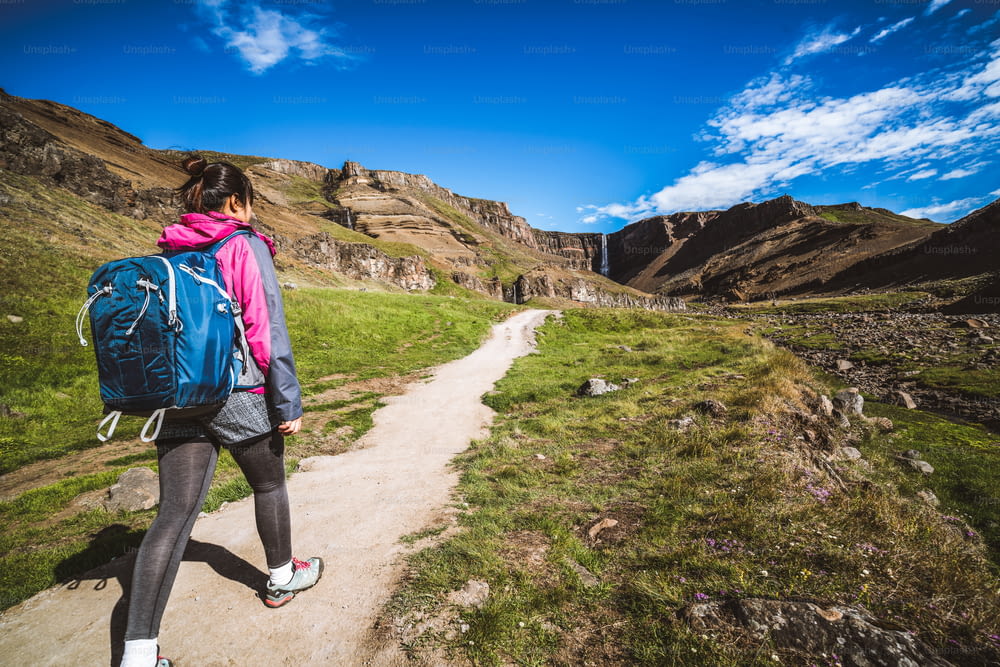 Woman traveler trekking in Icelandic summer landscape at the Hengifoss waterfall in Iceland. The waterfall is situated in the eastern part of Iceland.