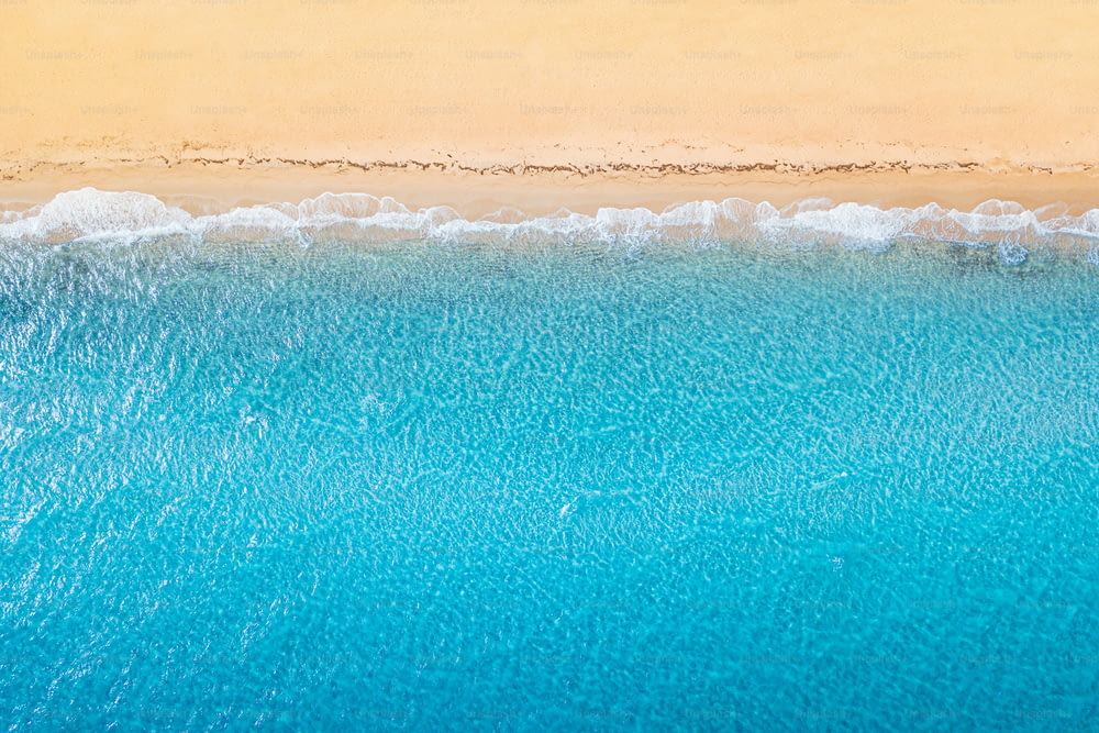 Vista aérea de una idílica playa de arena marina con olas azules y espacio de copia. El concepto de vacaciones en países tropicales y relajación. Antecedentes para viajes y vacaciones