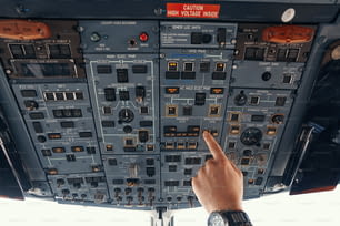 Piloto de avión que extiende la mano hacia el panel superior y alterna el interruptor para el control de la calefacción del parabrisas