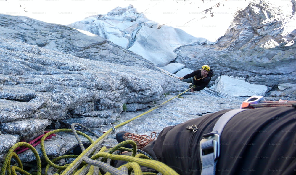 Alpiniste masculin en assurage lors d’une ascension classique difficile et exposée dans les Alpes suisses avec un glacier en contrebas