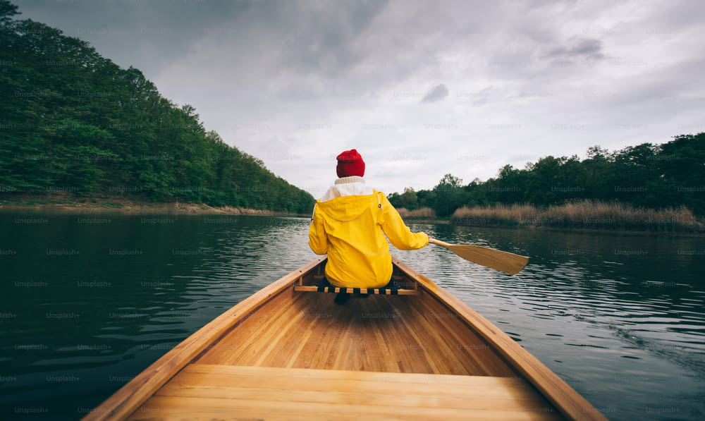 Rear view of woman in yellow raincoat paddling canoe. Enjoy canoeing