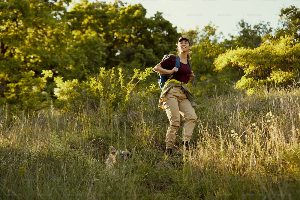 Young woman hiking with her dog in nature and moving down the hill.