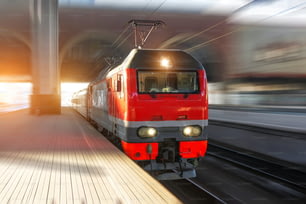 The lead electric locomotive with a passenger train passes at high speed through the city platform at the station