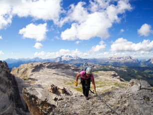 A female mountain climber reaches the summit with great Dolomites landscape behind