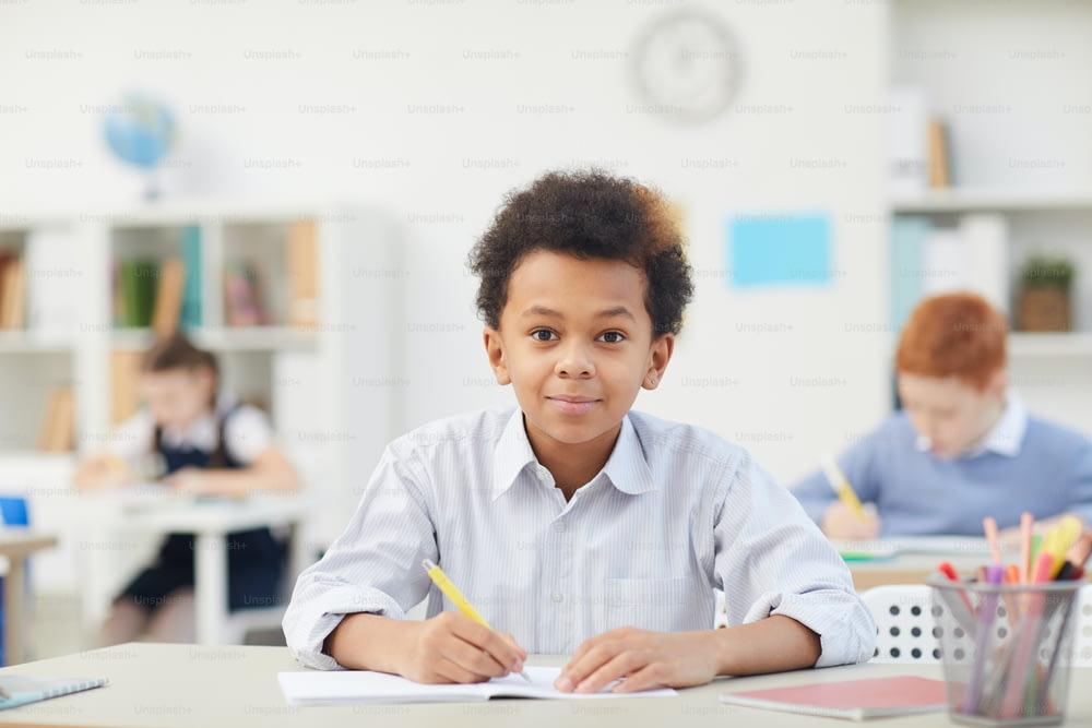 Ritratto di ragazzo africano seduto alla scrivania e guardando la macchina fotografica durante la lezione a scuola