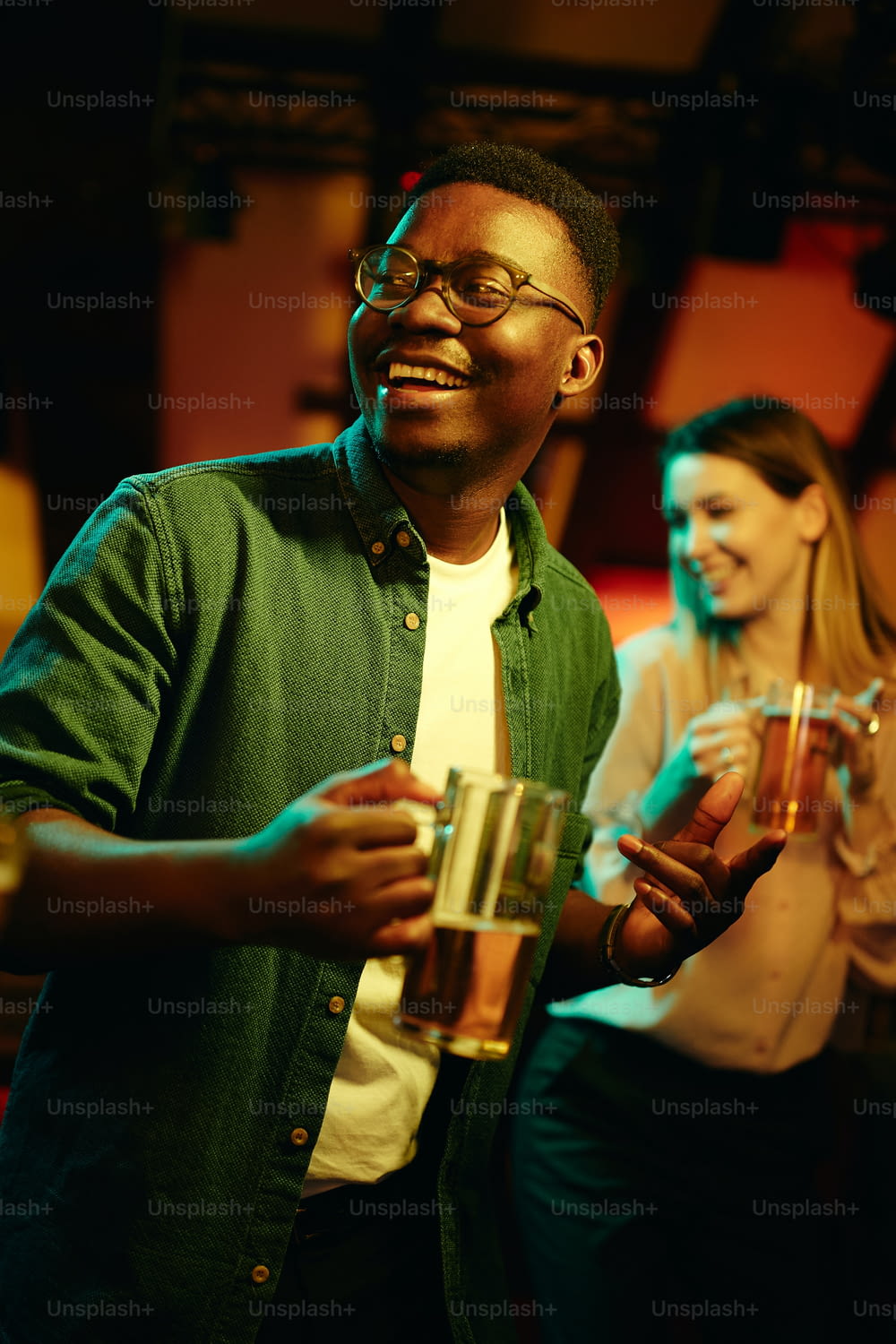 Glücklicher schwarzer Mann, der Bier trinkt und während der Nacht in einer Bar tanzt.
