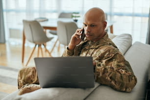 Veterano afroamericano usando una computadora portátil mientras habla por teléfono móvil en la sala de estar.