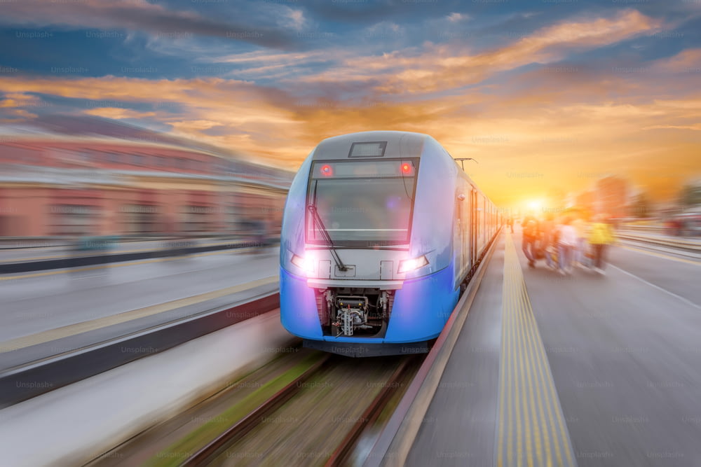 Railway station with modern high speed red commuter train with motion blur effect at colorful beautiful sunset