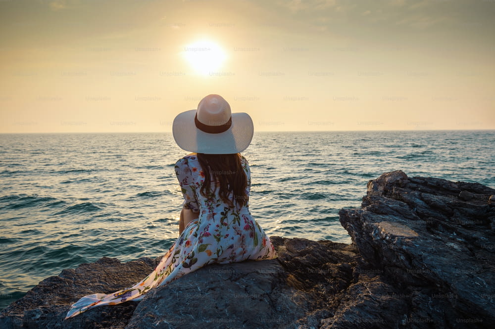 Jeune femme assise au sommet du rocher et regardant le bord de mer et le coucher du soleil sur l’île de Si Chang.