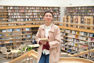 Porträt einer jungen Frau mit stehendem Buch in der großen Bibliothek