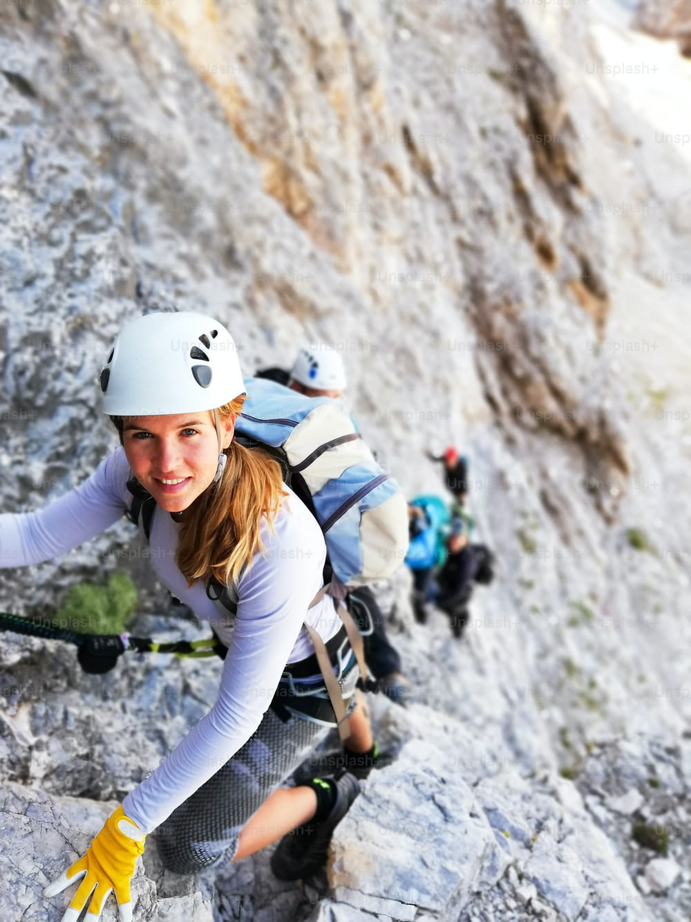 Horizontal view of an attractive blonde female climber on a steep Via Ferrata in the Italian Dolomites with a great view behind