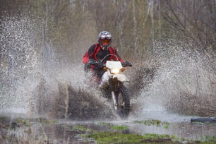 Motorcross rider racing in flooded wood and splashing big puddle on high speed