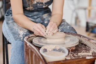 Primo piano di giovane artigiana creativa esperta in ceramica che crea un nuovo oggetto in argilla mentre è seduta con la ruota rotante in officina