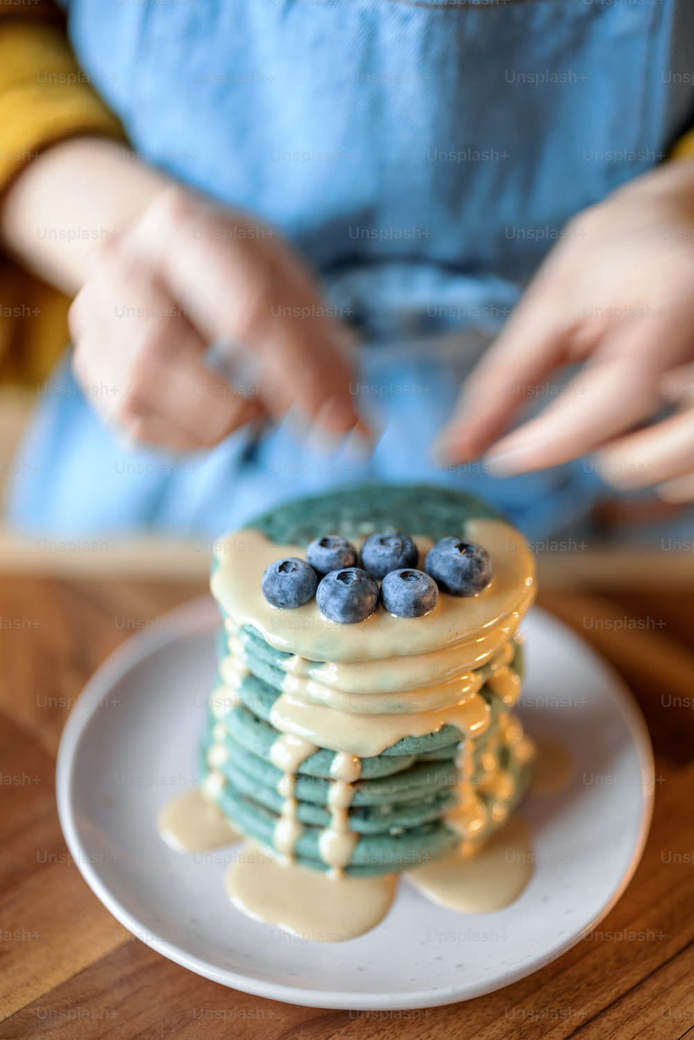 Woman in blue apron decorate blue american pancakes with blueberry poured with caramel souse on wood table. Homemade tasty food. Celebration of Shrovetide.