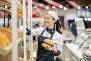 A saleswoman arranges bread and pastry on shelves at the supermarket.