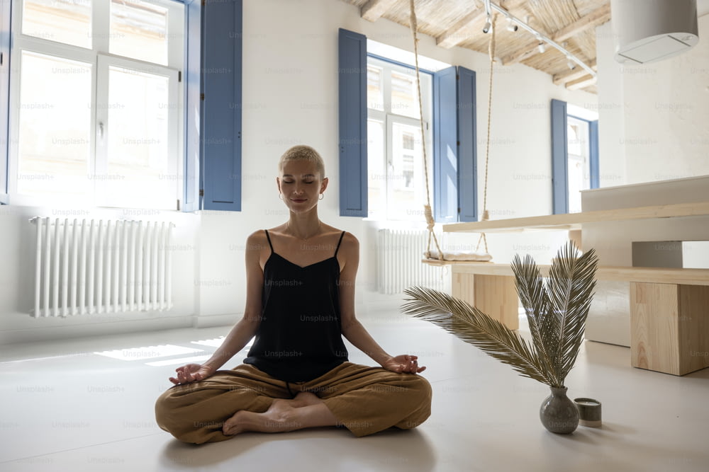 Giovane donna elegante che medita e pratica yoga in un moderno soggiorno luminoso a casa. Mindfulness, sentirsi tranquilli in una casa moderna