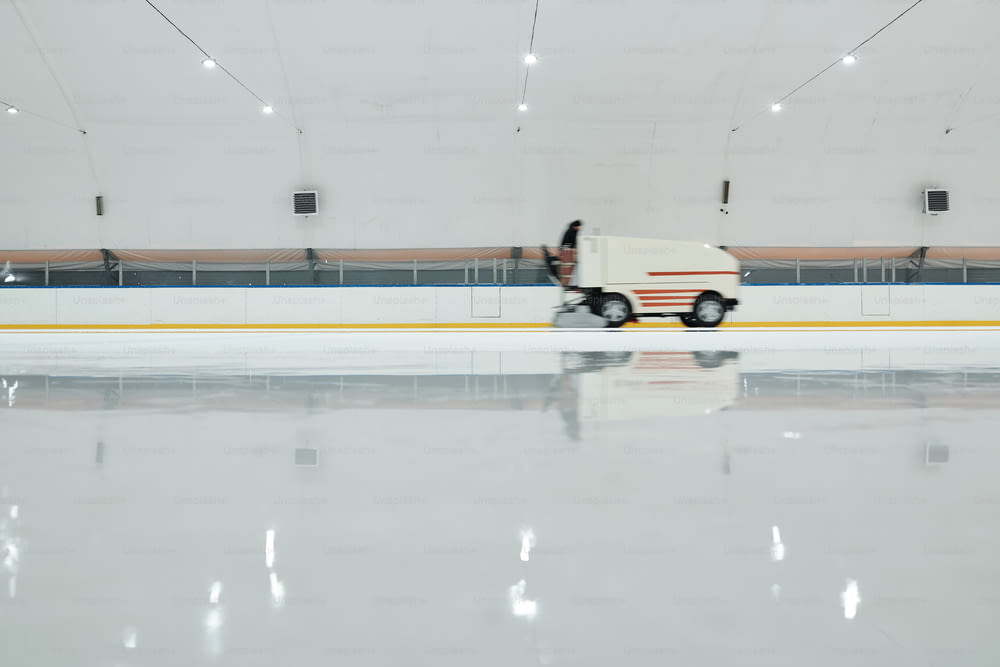 Weißer Lastwagen oder Eisabflachungsmaschine, der sich auf der Eisbahn bewegt, während er für das Hockeyspielen oder Schlittschuhlaufen im großen Sportzentrum vorbereitet wird