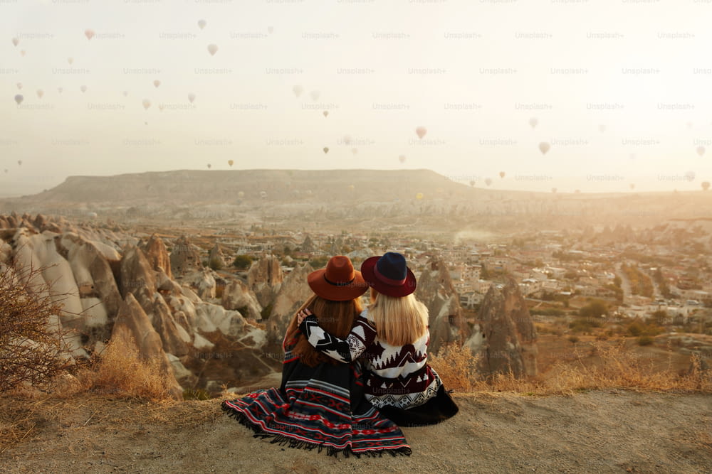 人々は旅行します。丘の上に座って帽子をかぶった女性が、カッパドキアトルコで熱気球の眺めを楽しんでいる。高解像度