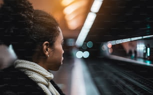 Vera vista laterale inclinabile di una giovane e bella donna afroamericana che guarda il treno in avvicinamento mentre si trova sulla piattaforma della stazione della metropolitana, con uno spazio di copia posto sulla destra per il tuo annuncio