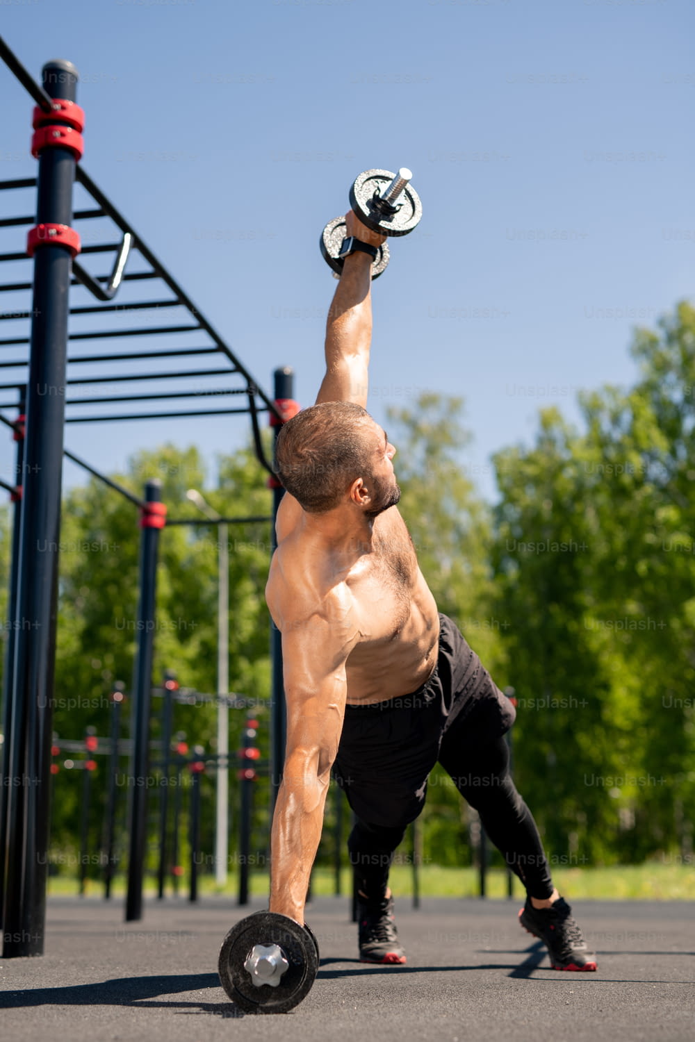 Giovane bodybuilder muscoloso che si allena all'aperto sul campo sportivo mentre solleva bilanciere pesante durante l'esercizio