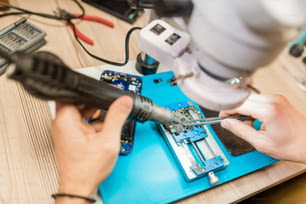 Utensile elettrico e pinzette nelle mani del riparatore che utilizza il microscopio durante il lavoro con piccoli dettagli dello smartphone smontato