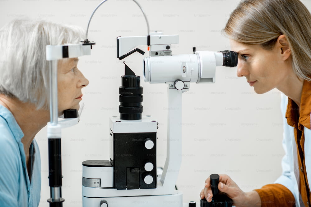 Oftalmólogo examinando los ojos de un paciente mayor usando un microscopio durante un examen médico en el consultorio oftalmológico