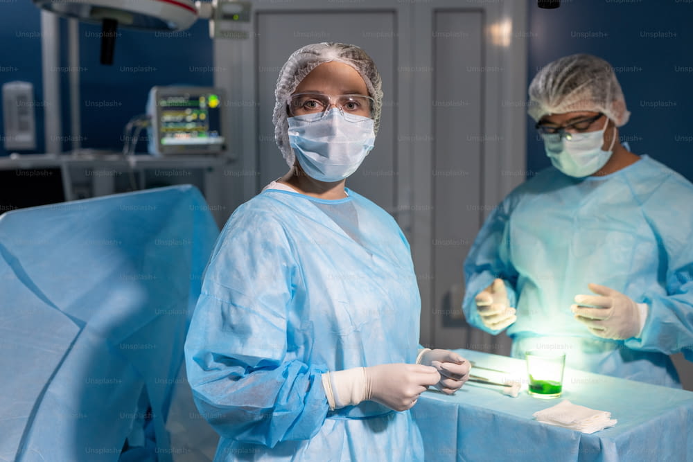 Chirurgienne professionnelle portant un masque de protection, des gants et des lunettes vous regardant contre son collègue masculin se préparant à l’opération