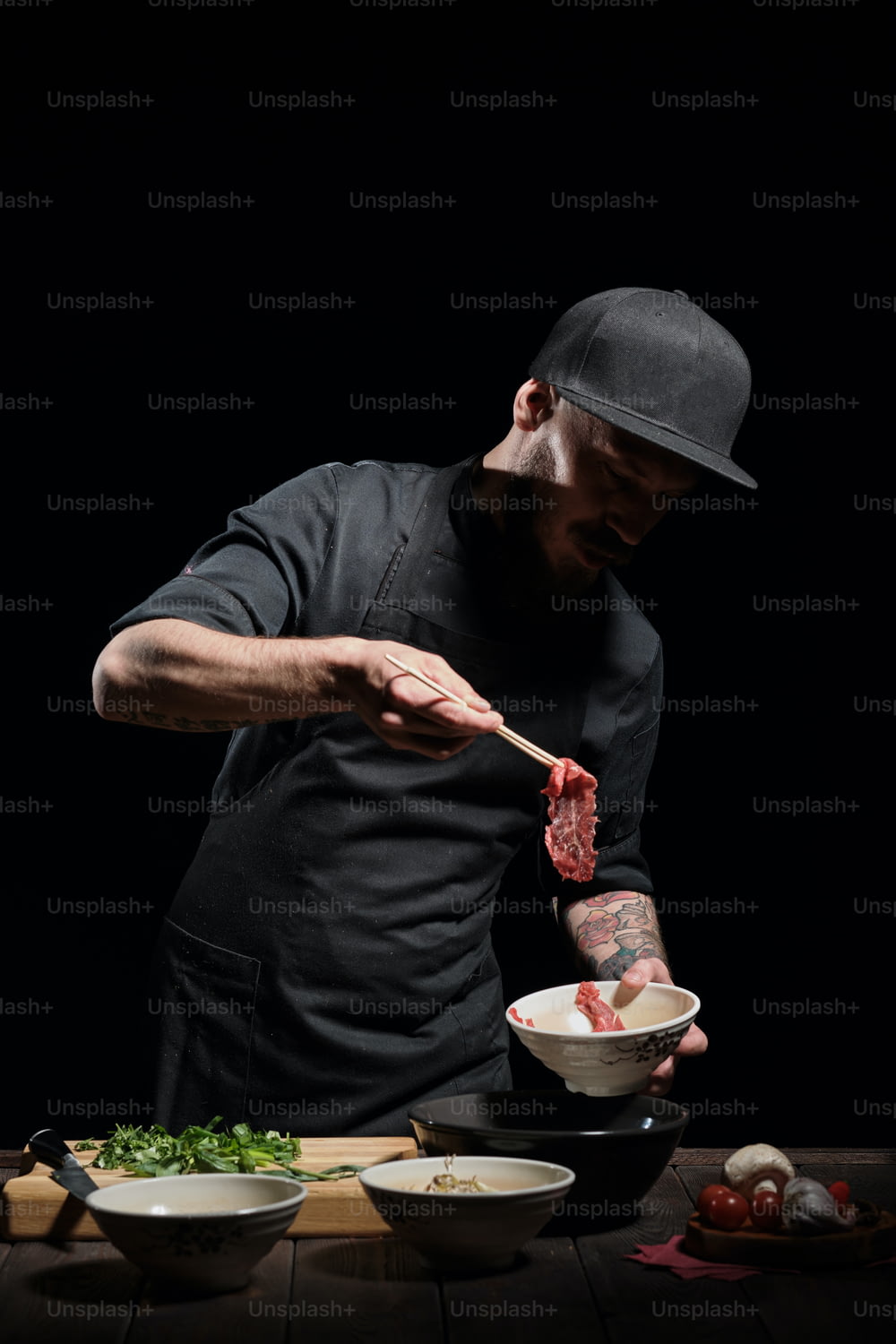 Porträt eines männlichen Kochs, der Fleisch mit Stäbchen in die Nudelschüssel gibt