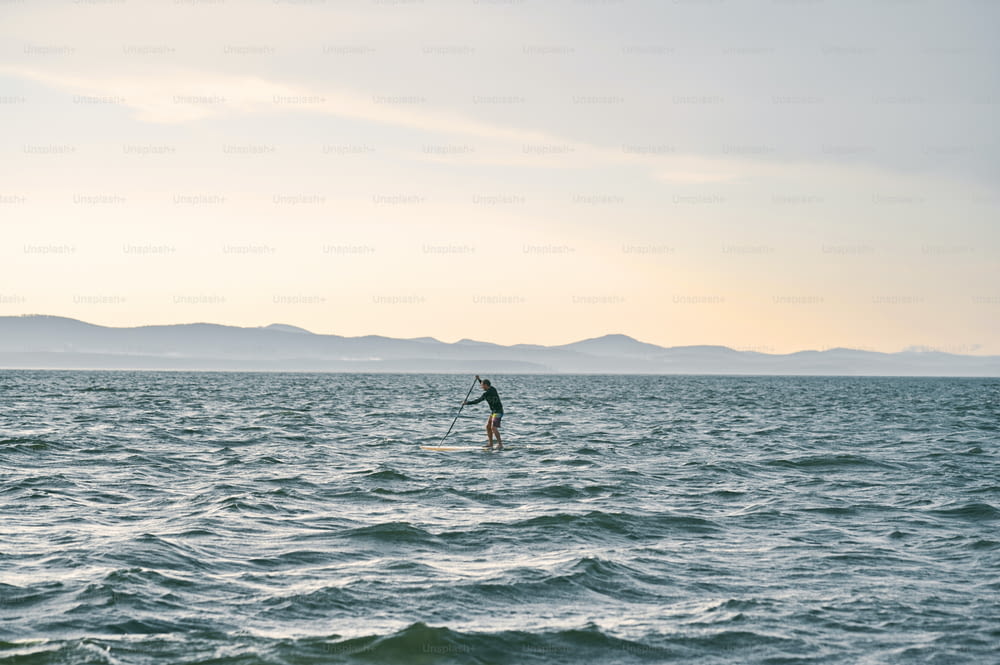 Petite figure d’un homme pagayant sur une planche de surf contre la nature sauvage ountain lake, vue panoramique