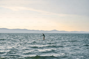 Small figure of a man paddling on a surf board against wild nature ountain lake, scenic view
