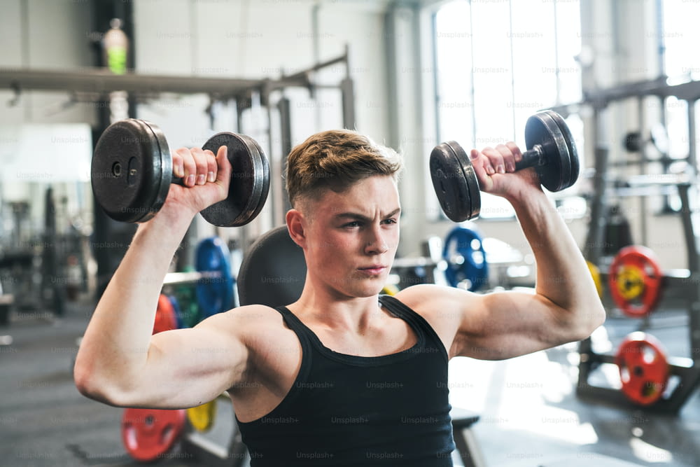 Young fit men doing strength training, exercising with dumbbells in modern gym.
