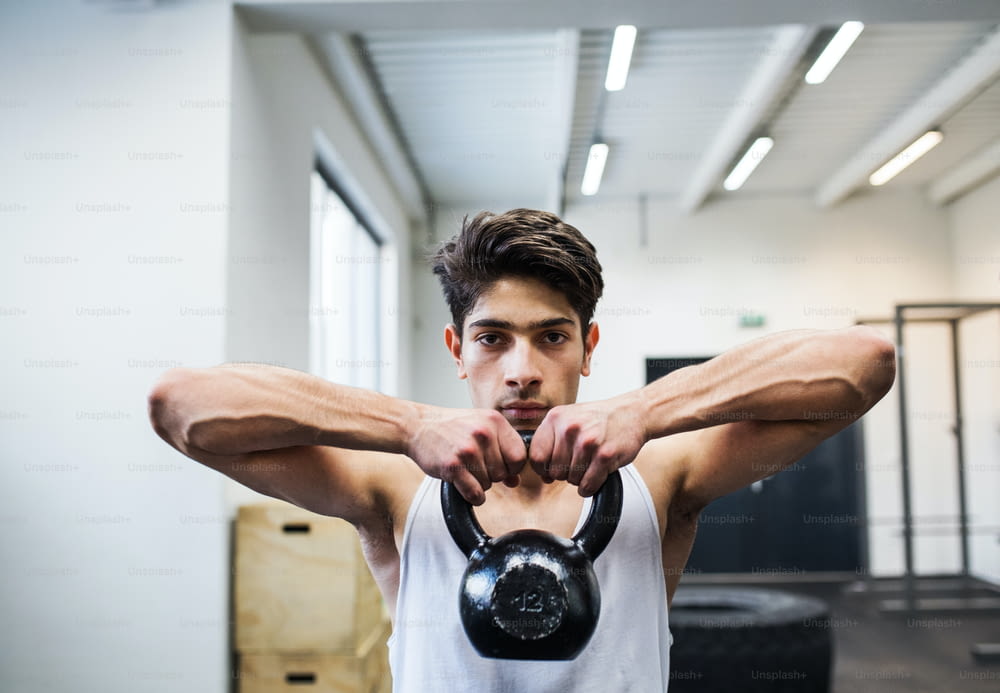 Fit hispanic man doing strength training, lifting kettlebell in gym.