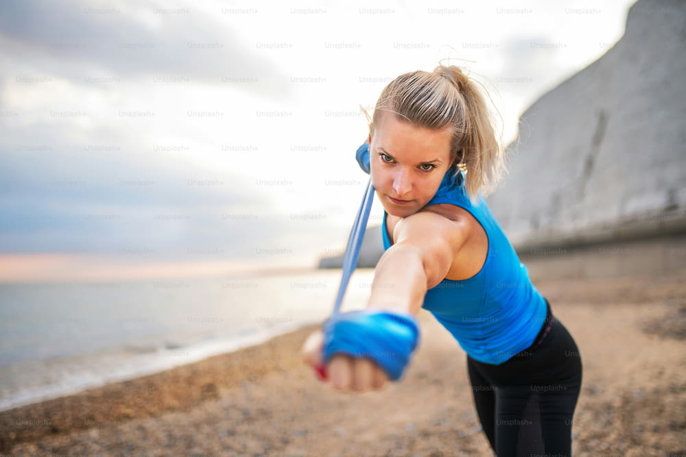 Jovem atleta corredora fazendo exercício com elásticos elásticos do lado de fora em uma praia na natureza. Espaço de cópia.