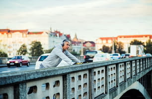 헤드폰을 끼고 프라하 시내의 다리 위에서 야외에서 음악을 들으며 건강한 남성 러너.
