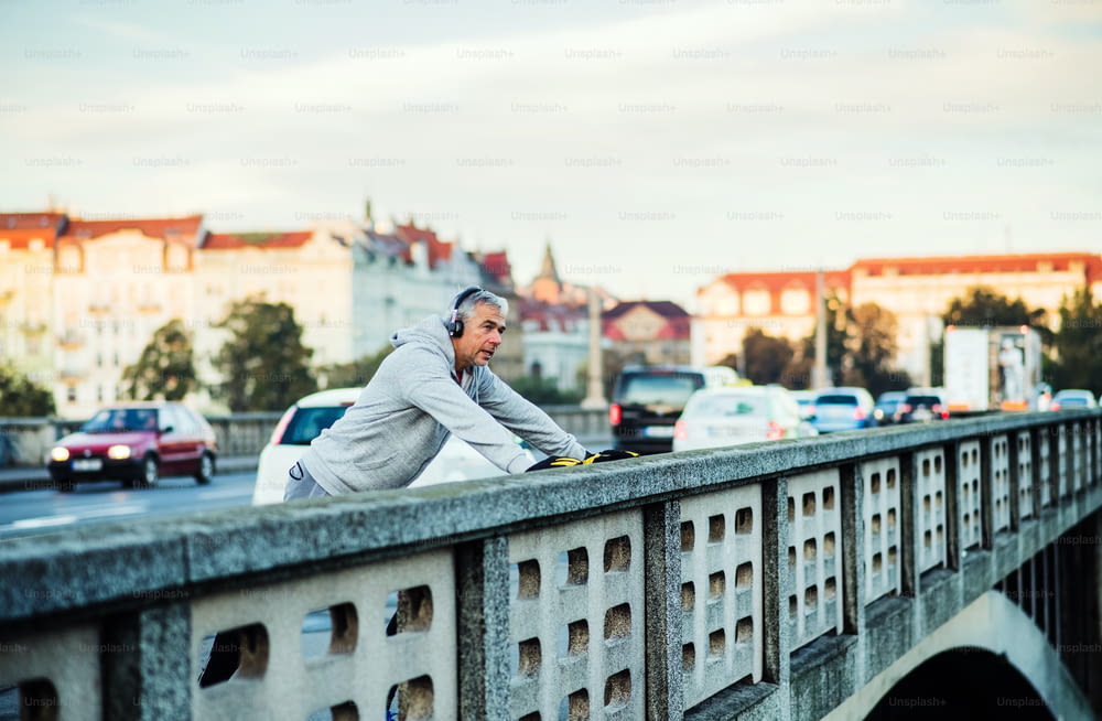 プラハ市内の橋の上で屋外で音楽を聴きながら、ヘッドフォンを装着した健康な成熟した男性ランナー。