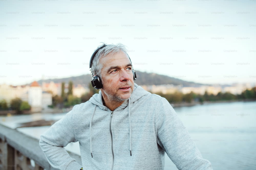 Mature male runner with black headphones outdoors on the bridge in Prague city, listening to music.
