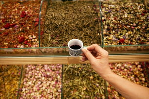 Hand With Cup Of Turkish Red Tea In Store Closeup, Assortment Of Tea On Background At Market. High Resolution