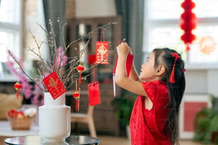 Süßes kleines Mädchen hängt handgemachte Postkarte mit Neujahrsgrüßen an Zweigen