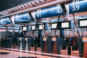 Interno dell'area check-in in un aeroporto moderno: terminal per l'accettazione dei bagagli con sistemi di trasporto a nastro per la movimentazione dei bagagli, più modelli di schermi LCD bianchi vuoti, banchi per il check-in indicizzati