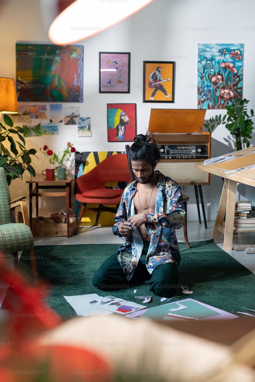 Kreativer junger Designer mit aufgeknöpftem Hemd sitzt zu Hause auf dem Boden und arbeitet an Collage, die Formen und Bilder ausschneidet