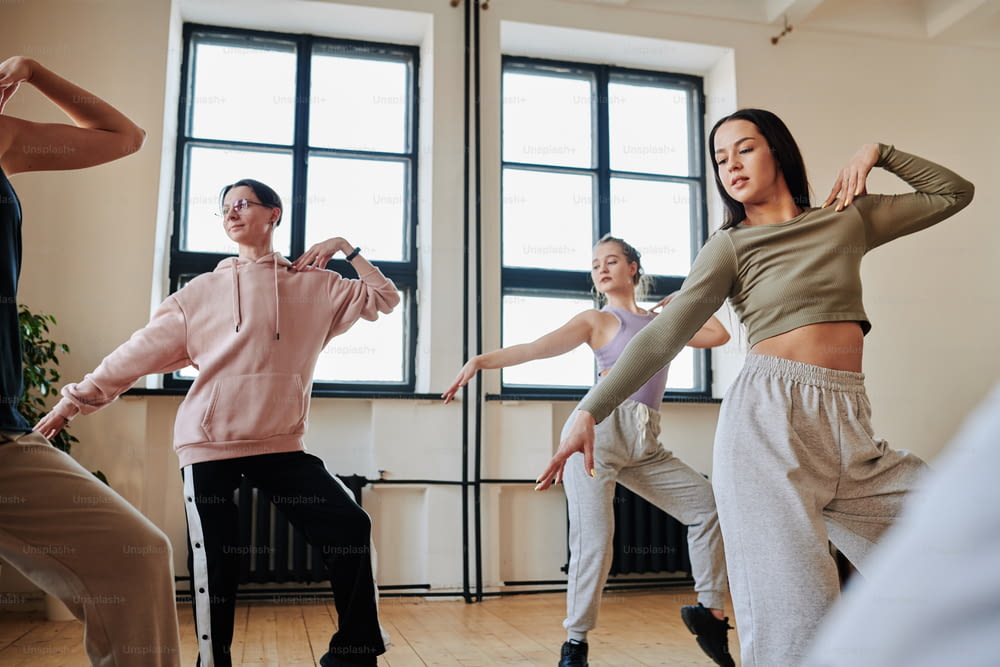 Grupo de adolescentes ativos contemporâneos praticando movimentos de dança da moda enquanto treinam no estúdio do loft ou no salão de dança