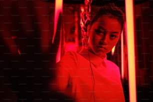 Retrato da jovem adolescente asiática com a mão em direção à câmera, em luz neon vermelha. Conceito de retrato cibernético e futurista