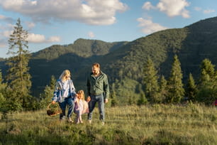 Young caucasian couple with little girl walk together while traveling in the mountains. Happy family spending summer vacation on nature