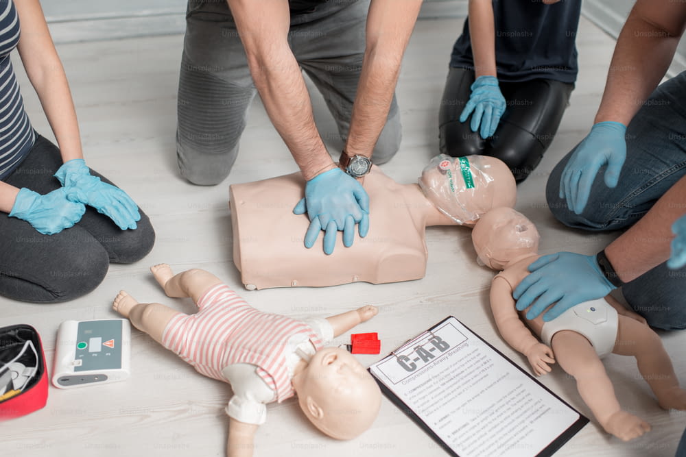 Group of people learning how to make first aid heart compressions with dummies during the training indoors. Close-up view on the hands and dummies